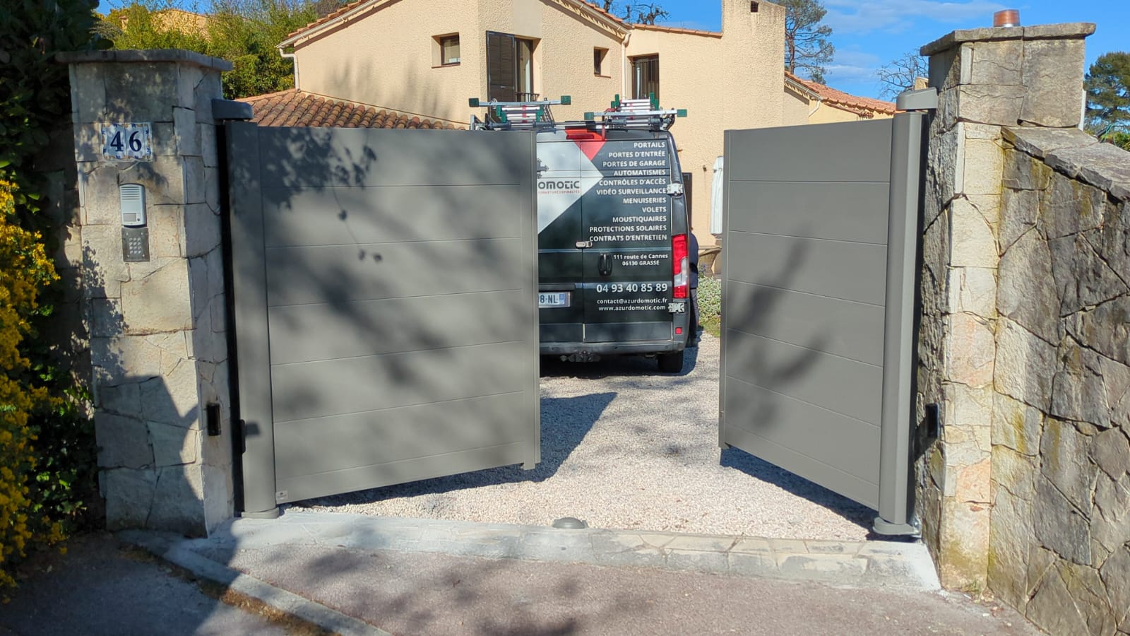 Portail battant aluminium anthracite Tschoeppe installé à Valbonne par Azur Domotic, vantaux ouverts sur allée de gravier