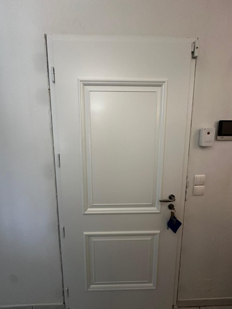 Vue intérieure d'une porte d'entrée aluminium blanc satiné avec poignée ton inox installée à Grasse