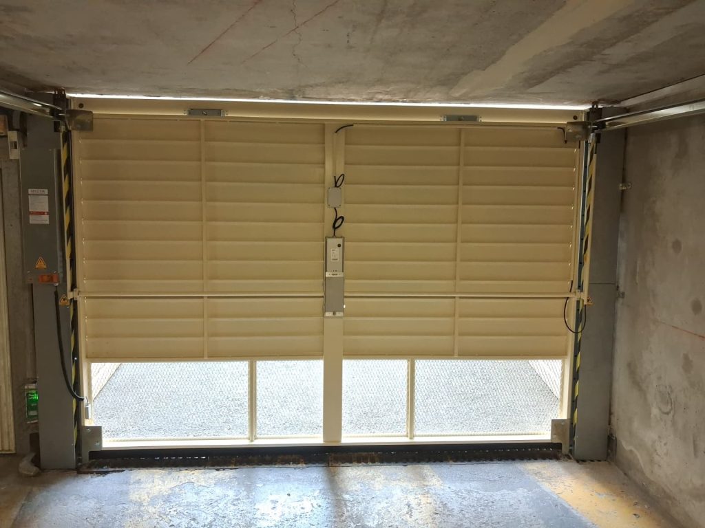 Porte de garage collective basculante SAFIR S424 AERO de coloris clair installee dans le parking souterrain d'une copropriete du Cannet