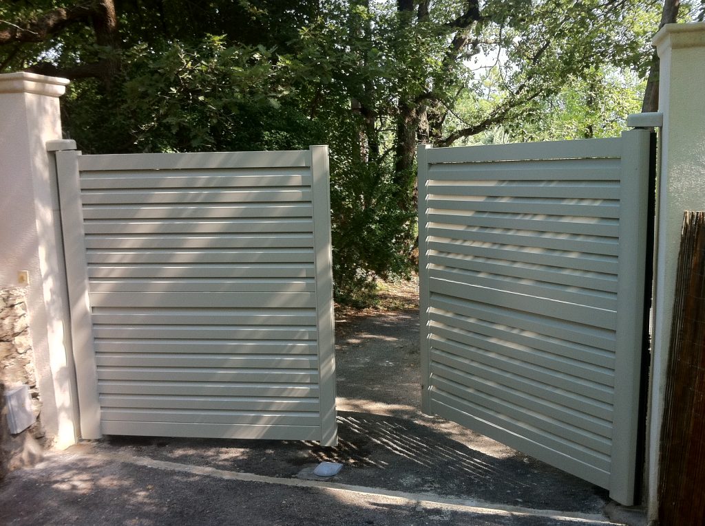 Portail battant aluminium Persia Tschoeppé entrouvert sur une allée gravillonnée à Saint-Paul-en-Forêt